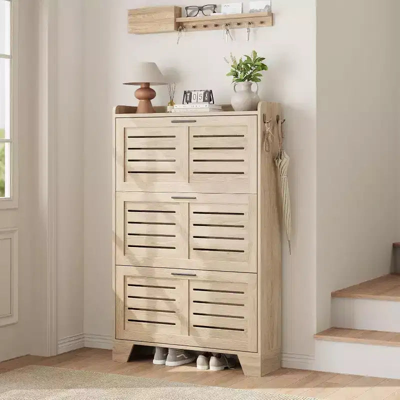 Meuble à chaussures autoportant avec 3 portes basculantes. Rangement dissimulé pour entrée, peut contenir plusieurs paires, style ferme avec crochets latéraux.
